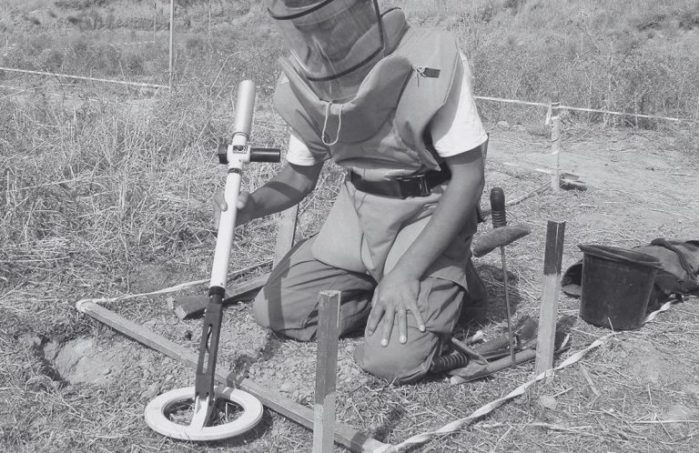 EOD operator using an Ebinger handheld detector to inspect an excavated target area.