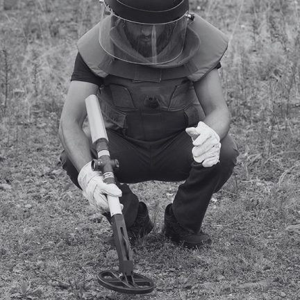 Deminer using TREX 210 MG metal detector during grassland mine clearance.