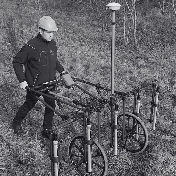 Operator using an Ebinger detector to conduct a UXO survey in wooded terrain.