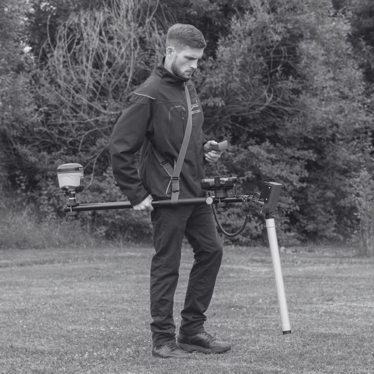 Operator using an Ebinger ground detector with integrated GPS during a UXO field survey.