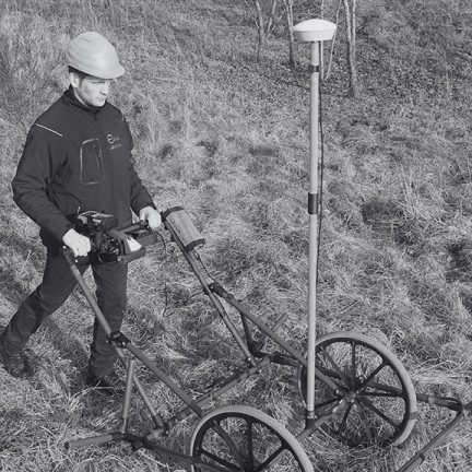 Operator using a wheeled Ebinger UPEX 740 M large-loop detector with GPS during a UXO survey.