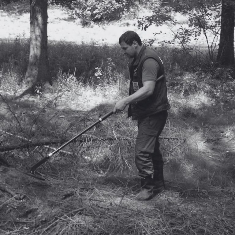 Operator using an Ebinger detector to conduct a UXO survey in wooded terrain.
